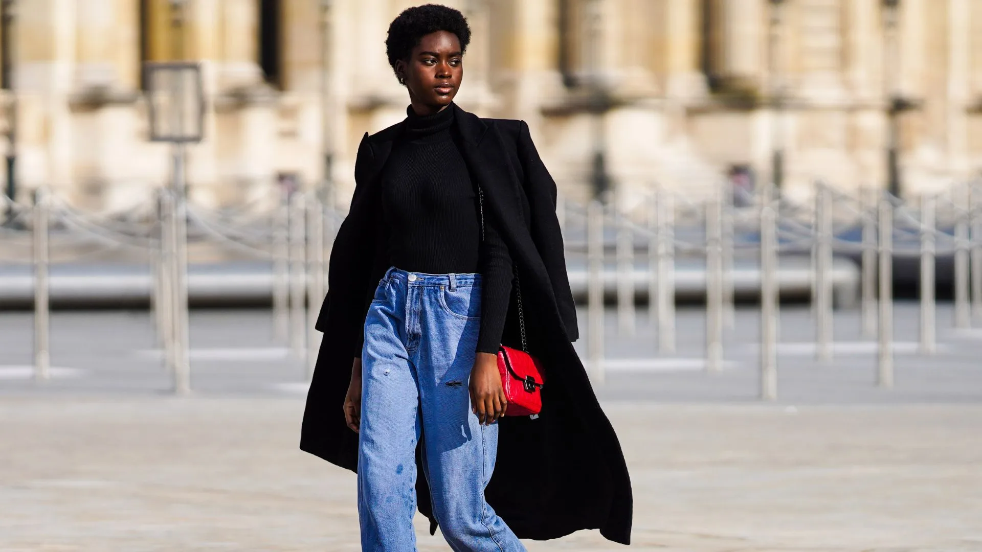 Girl wearing long black coat with jeans and a red bag
