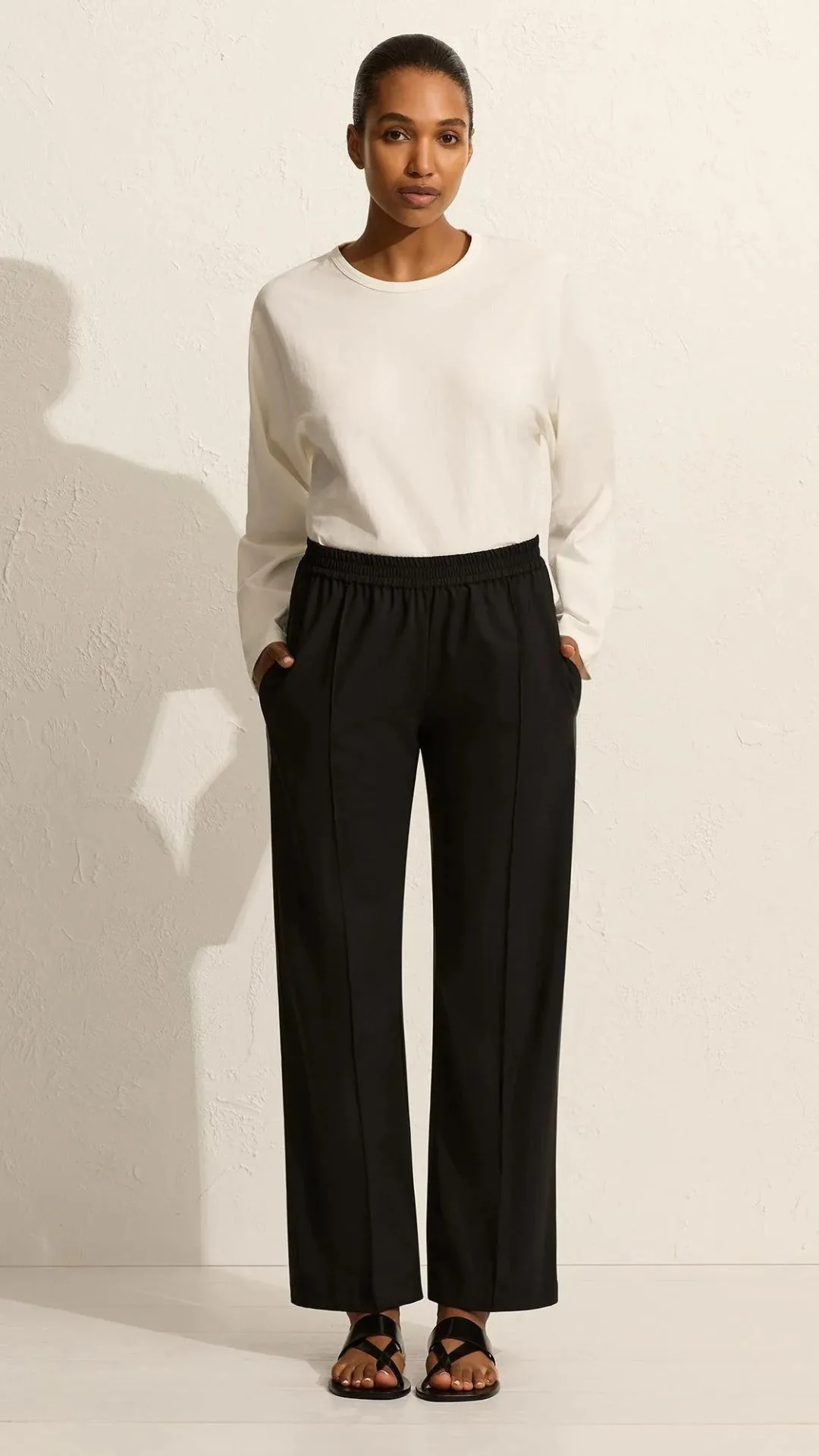 The Matteau Relaxed Pin-Stitch Trousers balance comfort and a relaxed fit with structured tailoring proving you don't need to sacrifice style for comfort when you're in trannsit. They feature a low elasticized wast with a pin-stich for structure and a loose, slightly flared leg. They are warn here with a long sleeve cream pull over and sandals. 