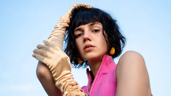 Portrait of a young beautiful freckled woman wearing gold satin gloves on sky background, fashion and retro style concept.