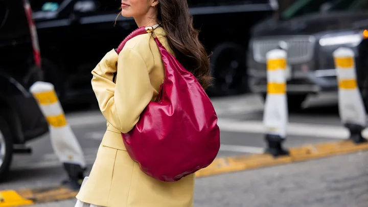 A guest wears yellow jacket, red bag, white skirt outside Altuzarra during New York Fashion Week