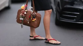 Livia Nunes Marques seen wearing Miu Miu navy blue polo shirt over a blue shirt, Miu Miu brown leather bag with colourful chains and charms, Rhode phone case, Miu Miu yellow underwear, blue shorts with green details and red flipflop shoes outside Miu Miu Show during the Womenswear Fall/Winter 2024/2025 as part of Paris Fashion Week on March 05, 2024 in Paris, France.