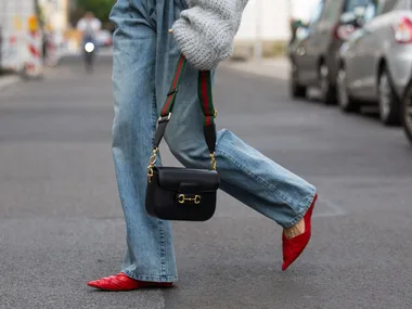 Lea Naumann wears grey asymmetric pullover / knit H&M, bag Gucci horsebit 1955, denim jeans Brunello Cucinelli, red pointed heels cos on May 05, 2024 in Berlin, Germany.