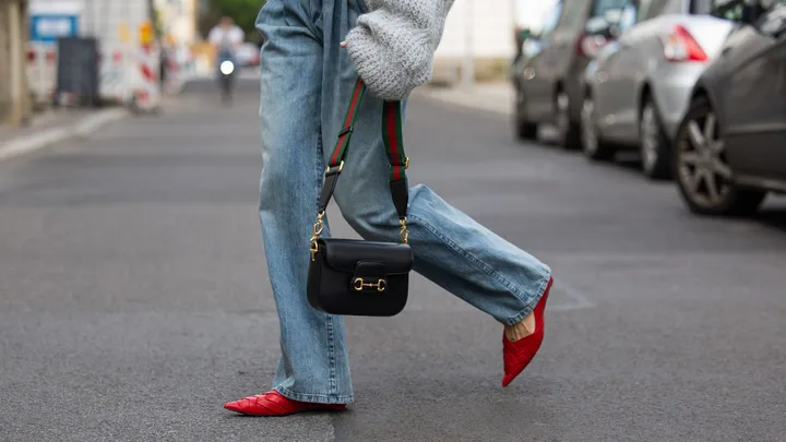 Lea Naumann wears grey asymmetric pullover / knit H&M, bag Gucci horsebit 1955, denim jeans Brunello Cucinelli, red pointed heels cos on May 05, 2024 in Berlin, Germany.