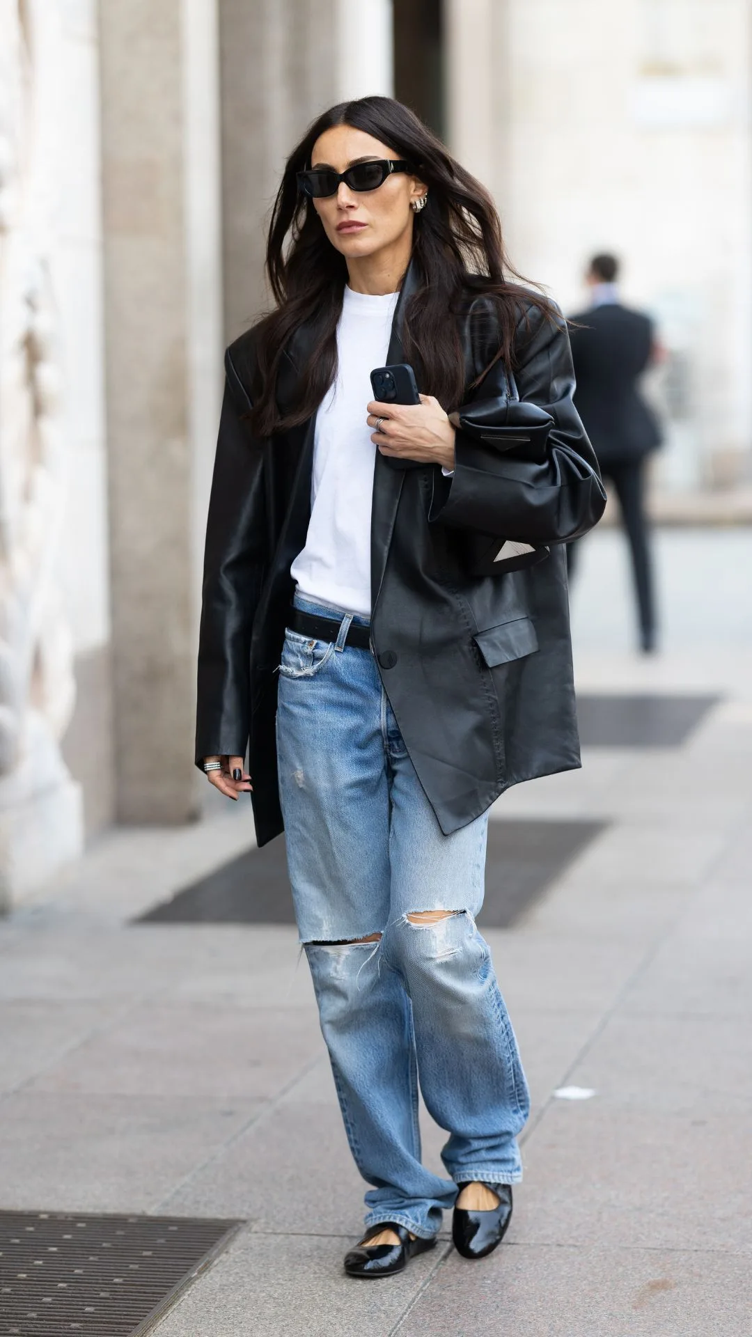 Giorgia Tordini wears black shiny leather ballerinas, silver hoop earrings, black sunglasses, a black belt, a black oversized leather jacket, a white oversized t-shirt and blue low waist straight jeans outside Andreadamo show during the Milan Fashion Week Menswear Spring/Summer 2025 on September 22, 2024 in Milan, Italy.