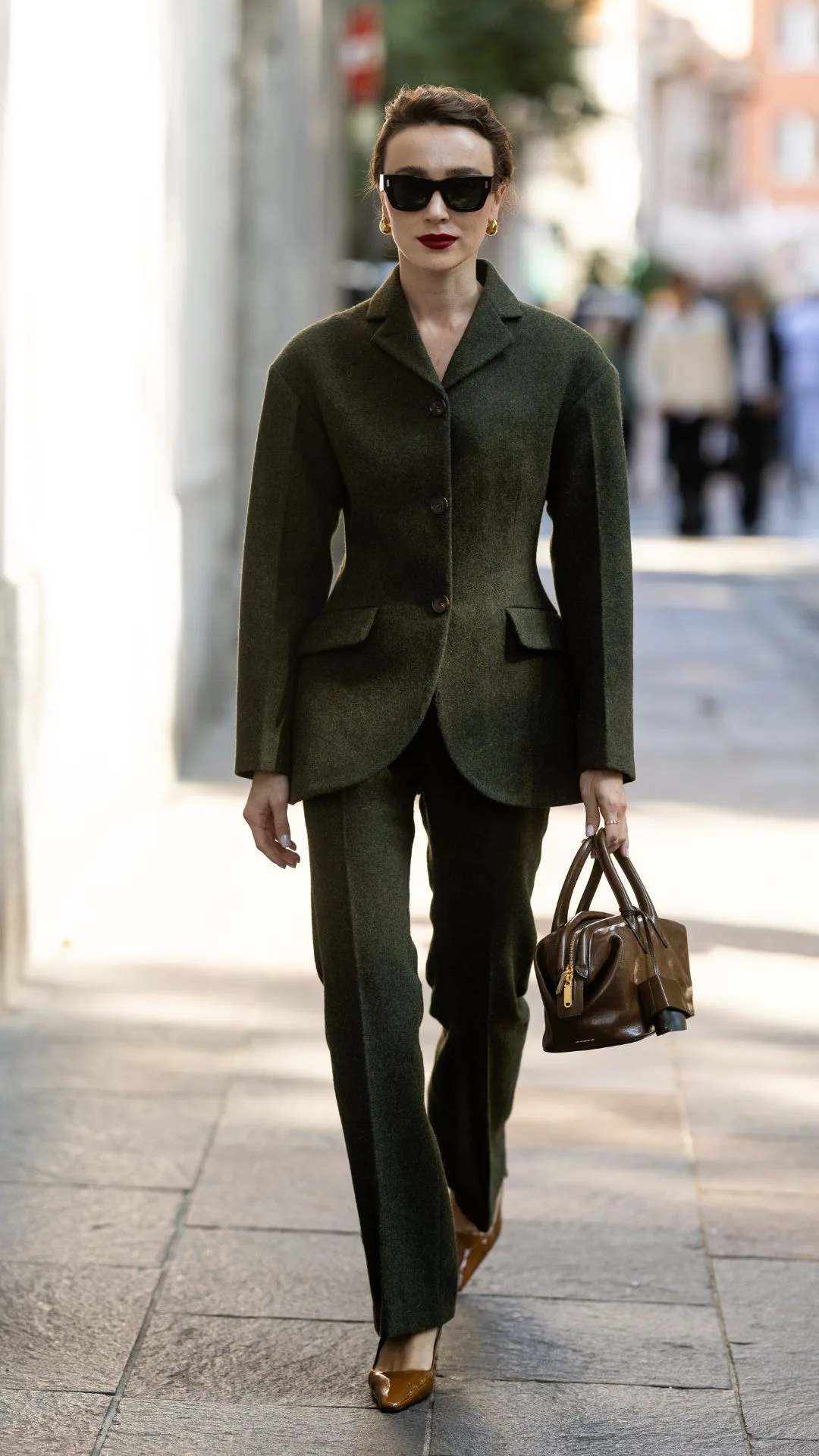 Mary Leest wears black sunglasses, a brown leather bag, brown leather pumps and a military green suit outside Bally show during the Milan Fashion Week Menswear Spring/Summer 2025 on September 21, 2024 in Milan, Italy.