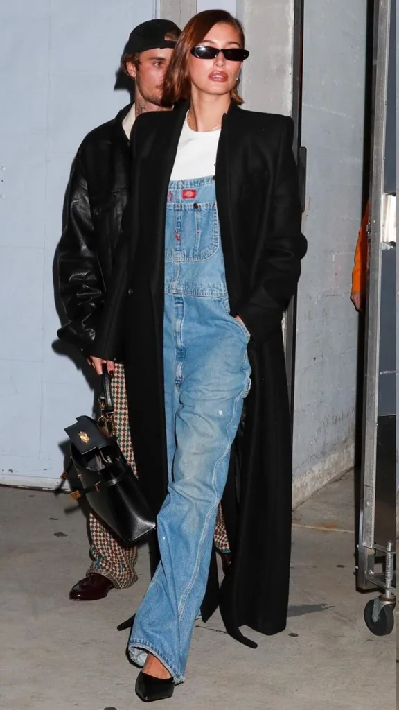 Hailey Bieber wearing Dickies denim overalls with a long coat and heels