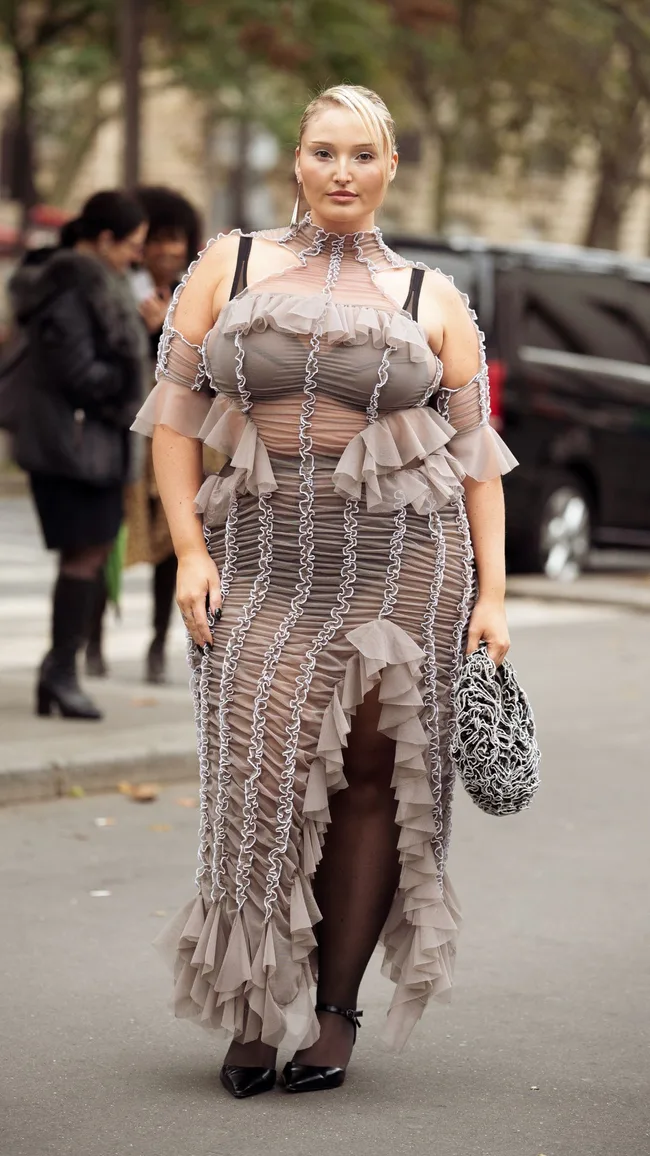 a street style photograph of a woman wearing a ruched sheer dress at paris fashion week