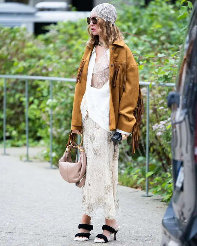 woman at paris fashion week wears brown leather jacket over white dress with sunglasses lace head scarf and heels