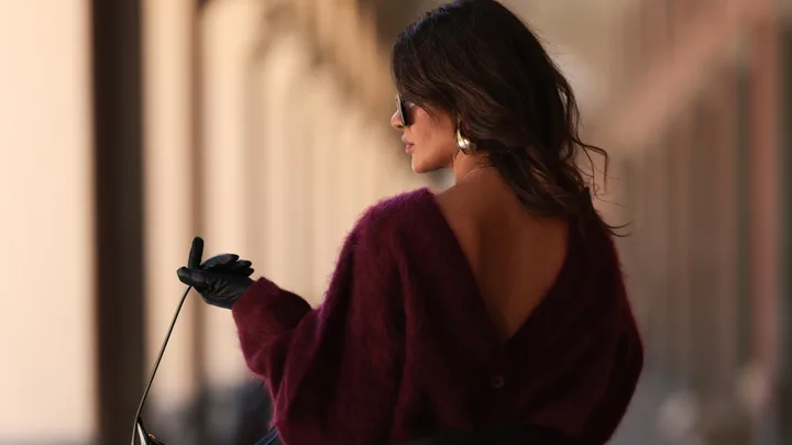 A stylish woman with wavy hair holding a bag and looking over her shoulder.