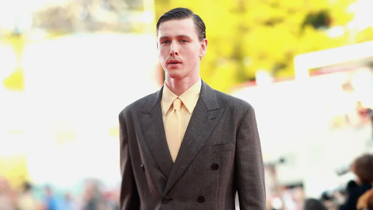 harris dickinson wears a suit with yellow shirt