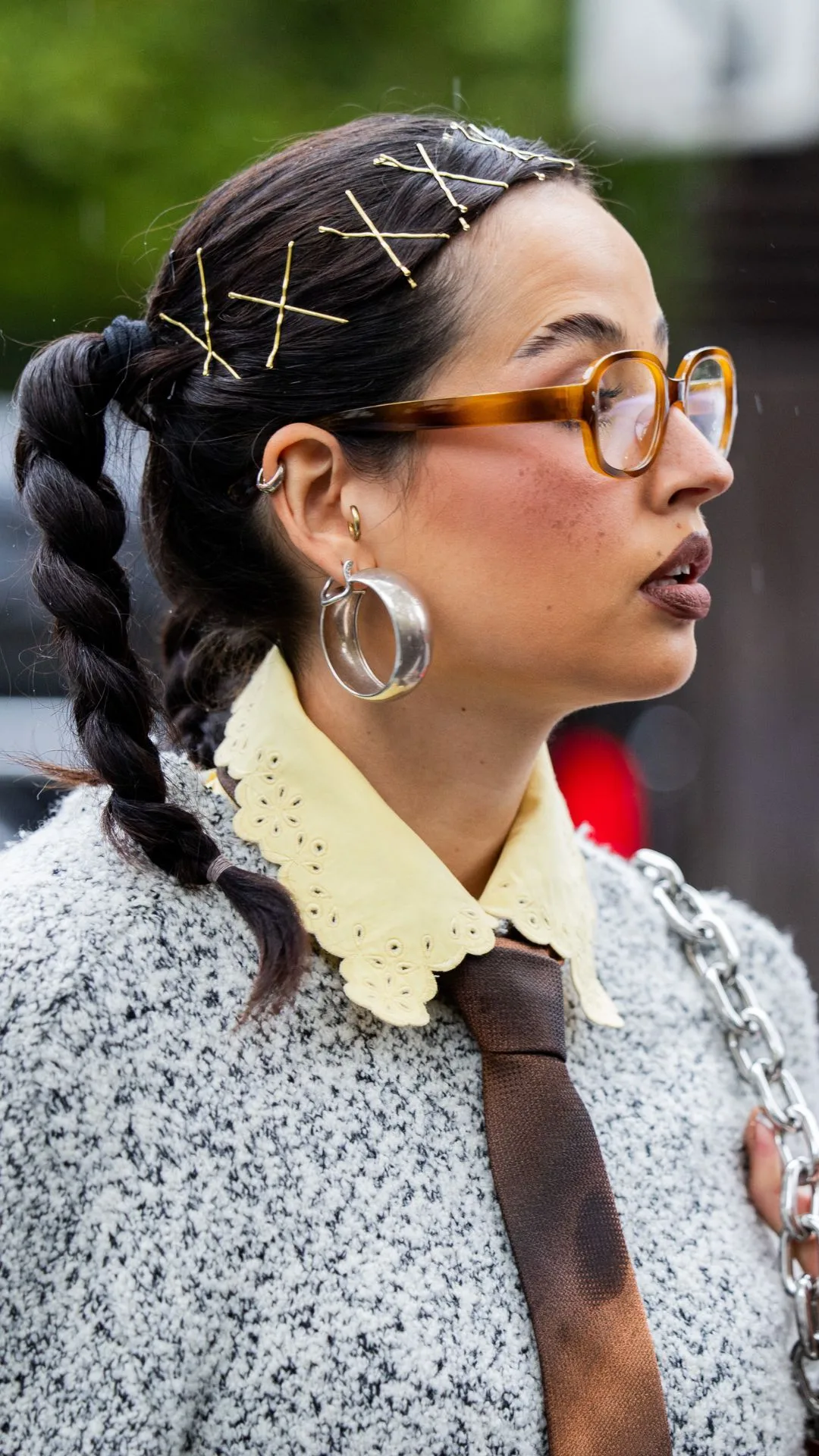 A guest wears hair clips brown tie, grey knit, glasses, earrings outside Rabanne during Womenswear Spring/Summer 2025 as part of Paris Fashion Week on September 25, 2024 in Paris, France.