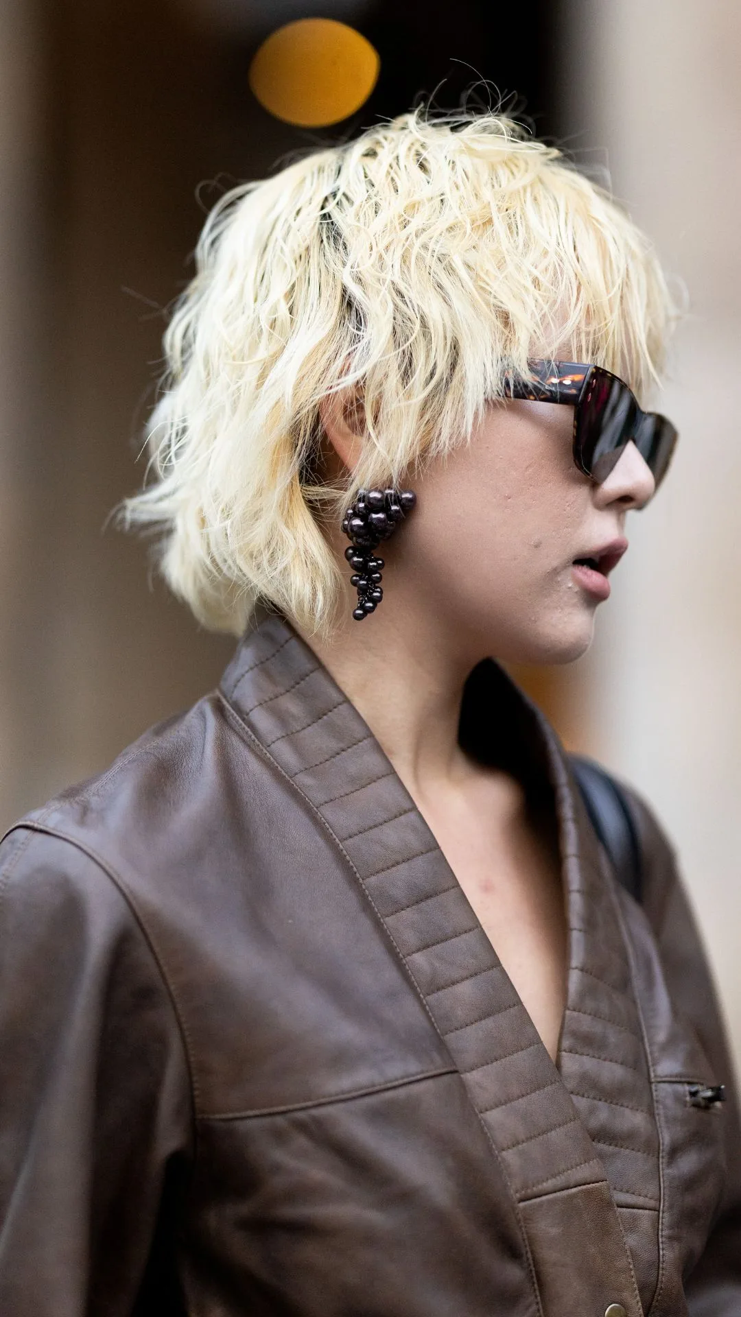 A guest wears brown sunglasses, black pearls pendant earrings and a brown leather long sleeved jumpsuit outside Isabel Marant show during Womenswear Spring/Summer 2025 as part of Paris Fashion Week on September 29, 2024 in Paris, France. 