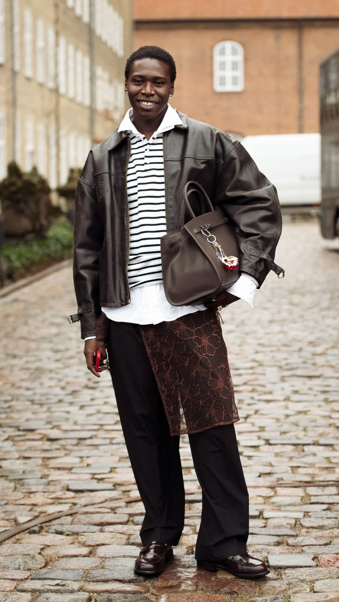 copenhagen street style fashion week autumn winter 2025 woman wears brown lace skirt over trousers with leather jacket and striped shirt