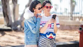 A woman on her phone at fashion week, her friend looks over her shoulder.