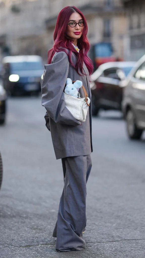 A guest at Paris fashion week wearing a grey suit with a teddy bear in her handbag