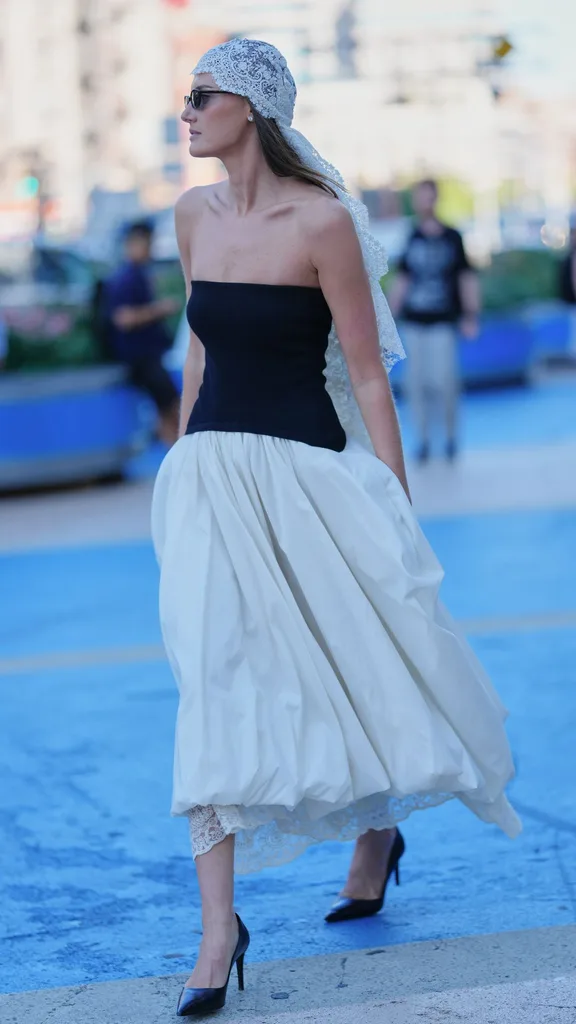 Guest at nyfw wears drop waist dress with cream balloon skirt and white lace headscarf