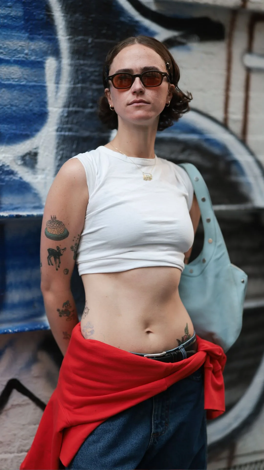 Guest at nyfw wears white midriff top with read sweater wrapped around waist 
