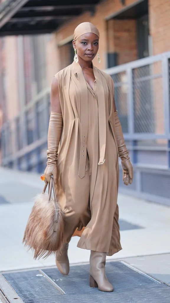 Guest at nyfw wears full beige 70s style jumpsuit with matching head scarf and faux fur handbag