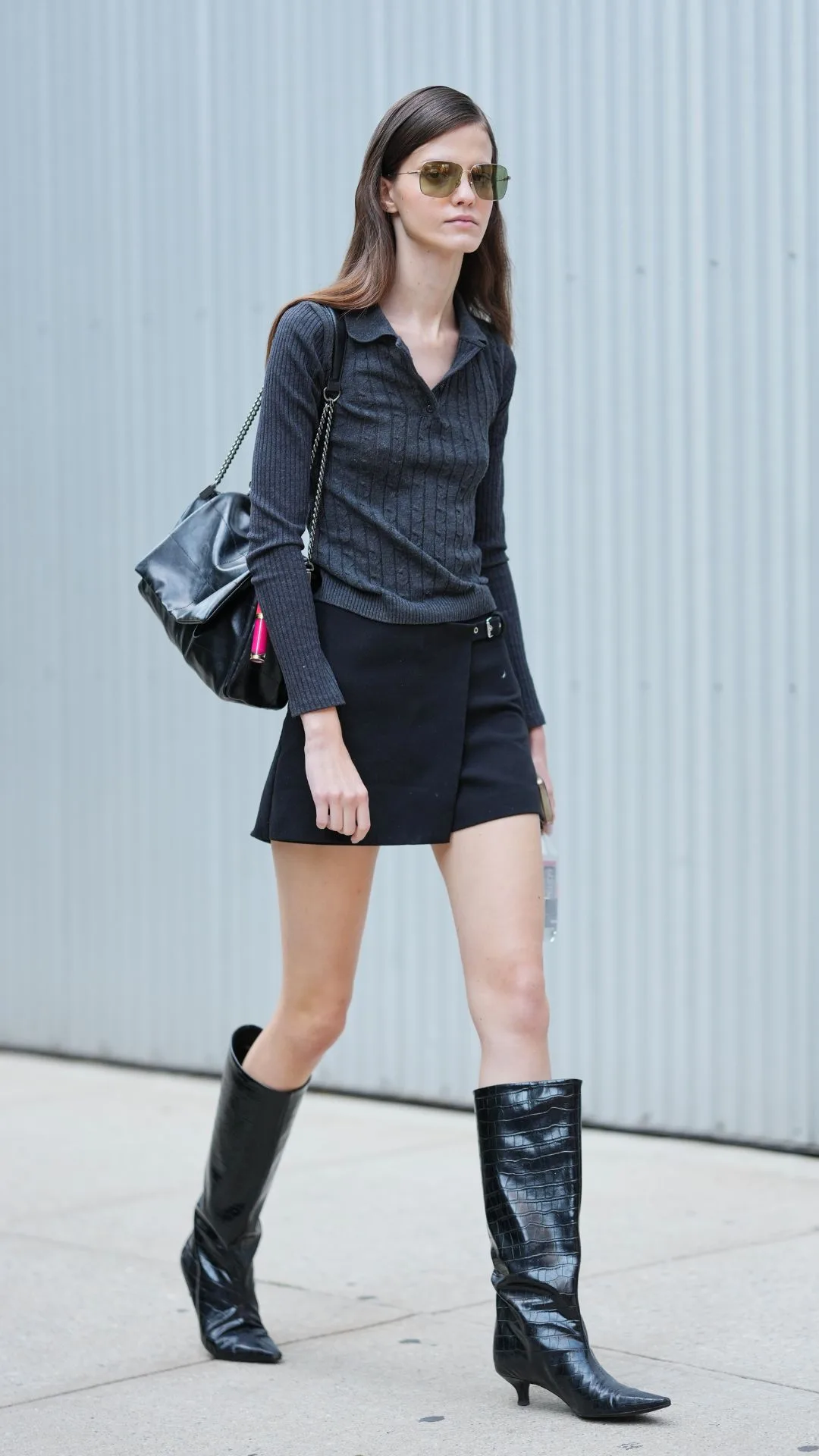 Model leaving show wearing black mini skirt with calf length boots and long sleeve grey top 