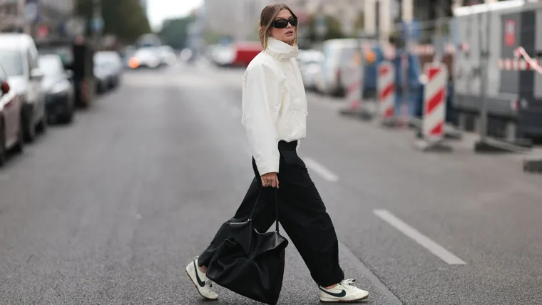 Stylish woman wears black and white sneakers with black trousers, white shell jacket and black, shiny leather tote bag
