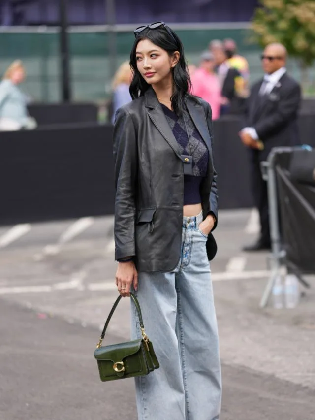 Stylish woman in leather jacket and jeans carries forest green leather coach handbag with gold C logo