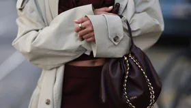 Stylish woman in trench coat and Loewe pouch bag wears gold oura ring