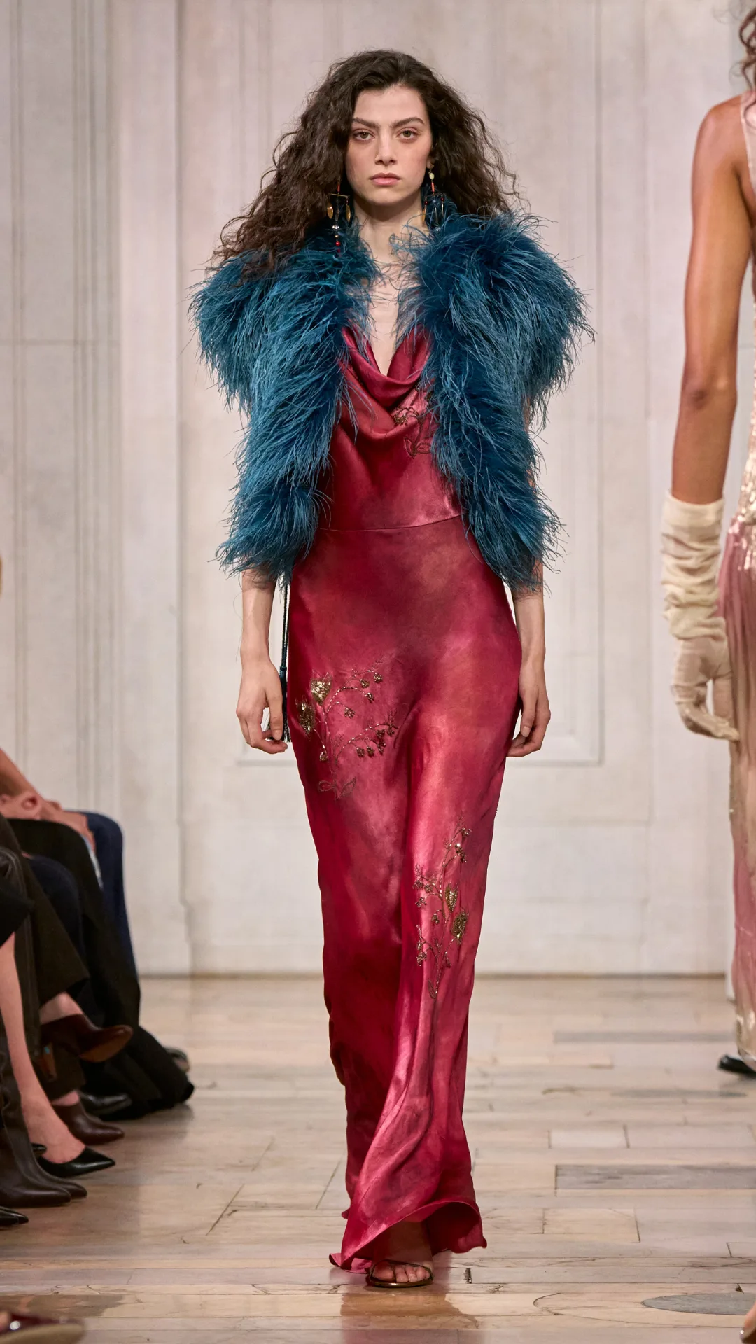A look from the Ralph Lauren show with the model wearing a crimson slip dress and a teal feather vest.