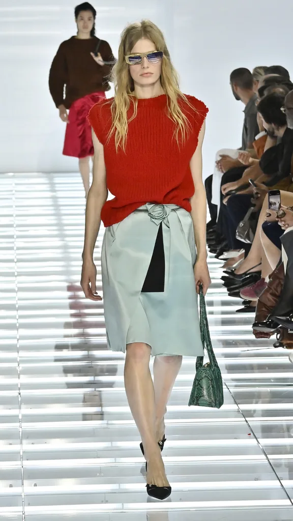 A model in a red top and light blue skirt