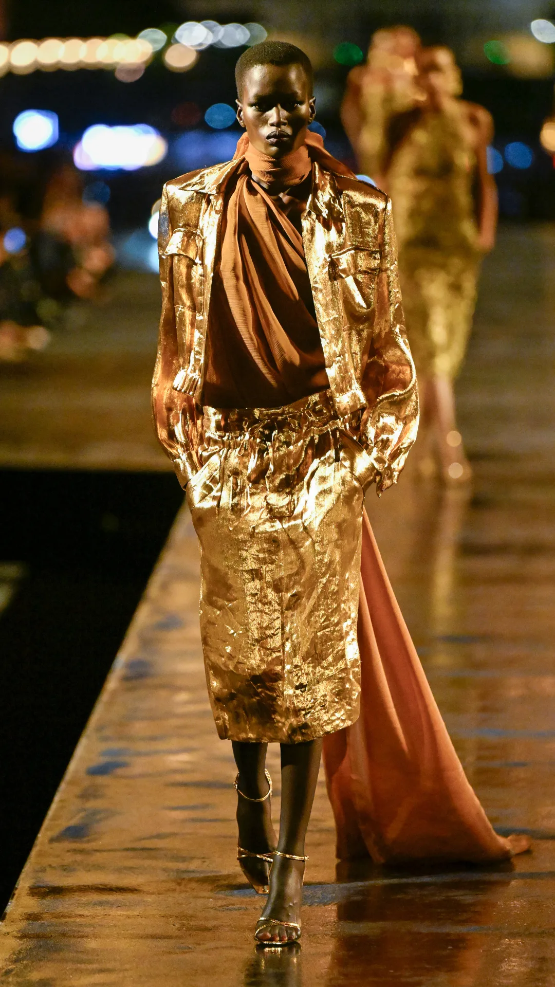 A model wearing a gold skirt and jacket with brown top