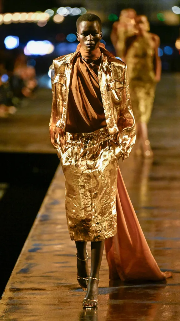 A model wearing a gold skirt and jacket with brown top