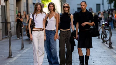 Four women wearing different coloured denim jeans pose for the camera on the street at fashion week