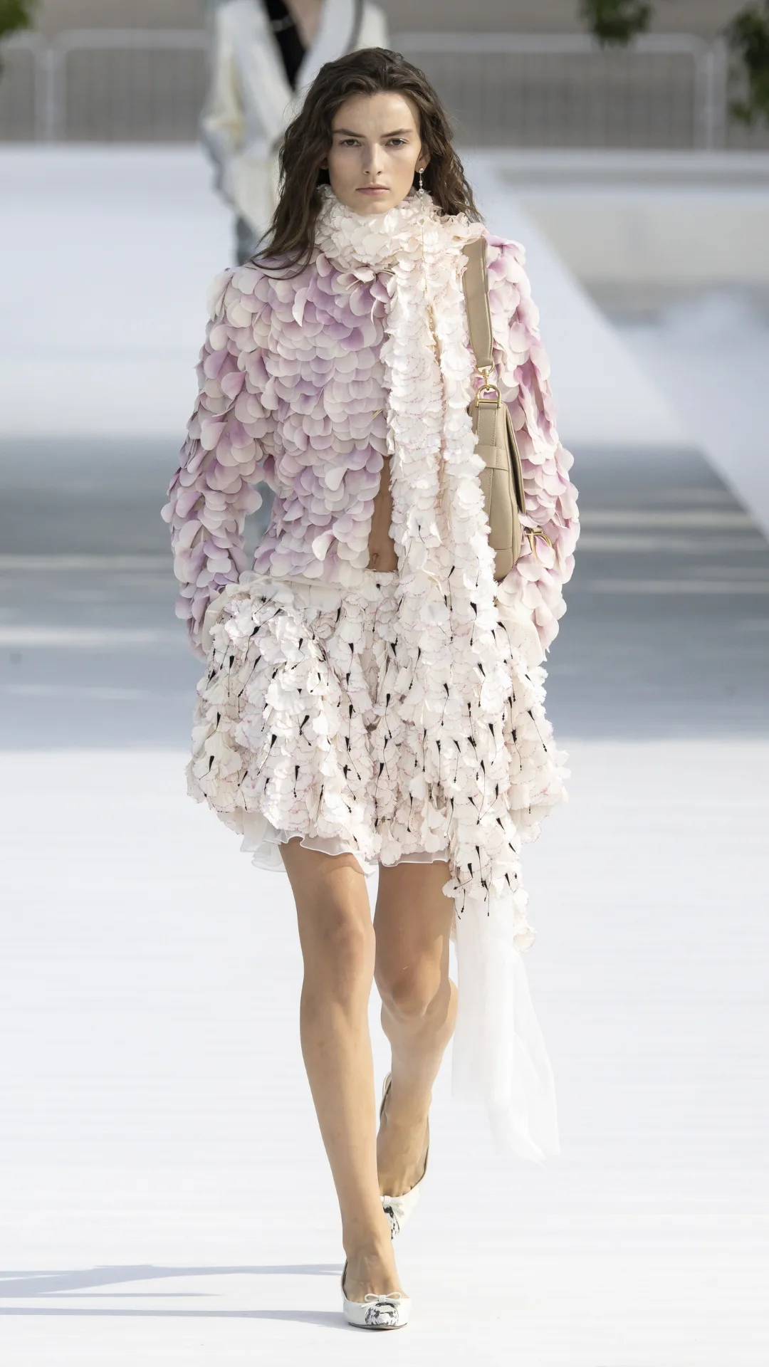 A model wears a petal-covered jacket and skirt