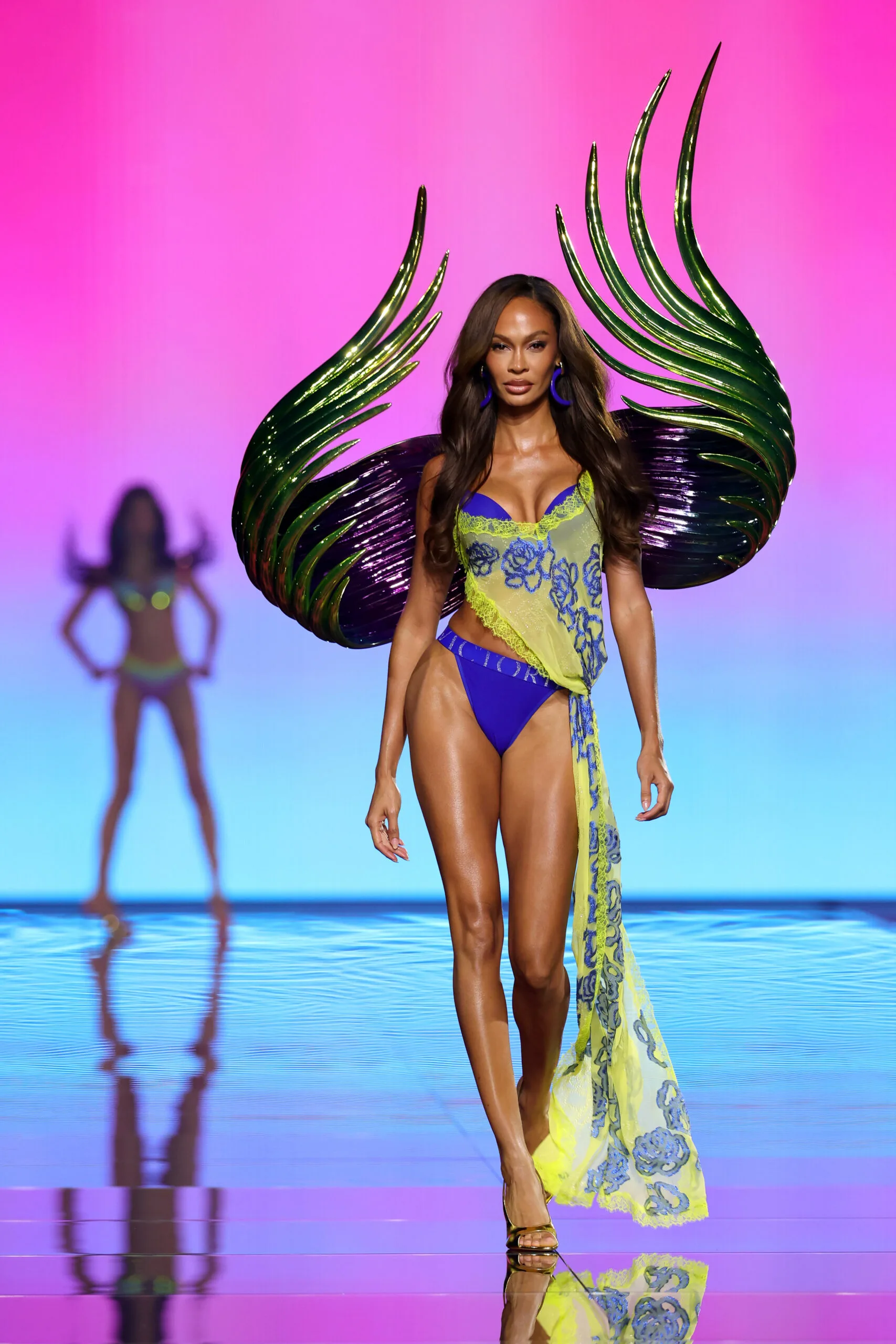Joan Smalls walks in blue and acid yellow lingerie with sharp metallic green and purple sculptural wings