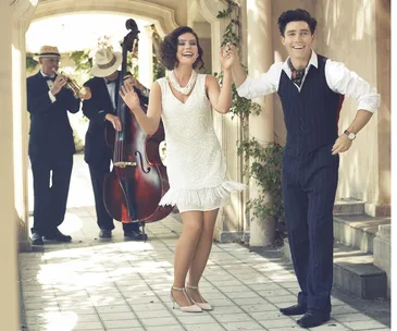 A couple dances joyfully in 1920s attire, while a jazz band plays in the background, featuring trumpet and double bass.