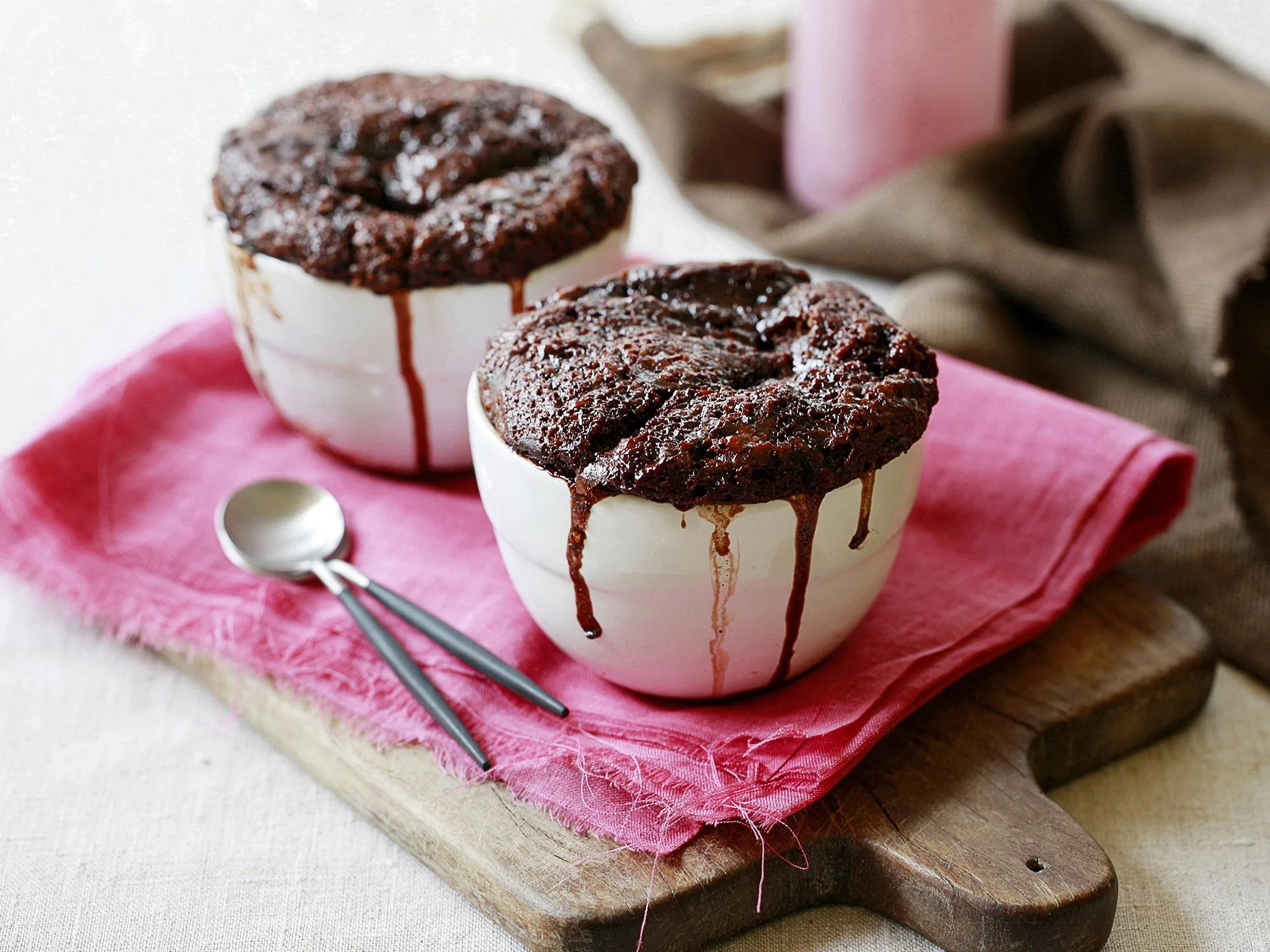 Two chocolate lava cakes in white bowls on pink cloth with spoons, perfect for Mother's Day treat.