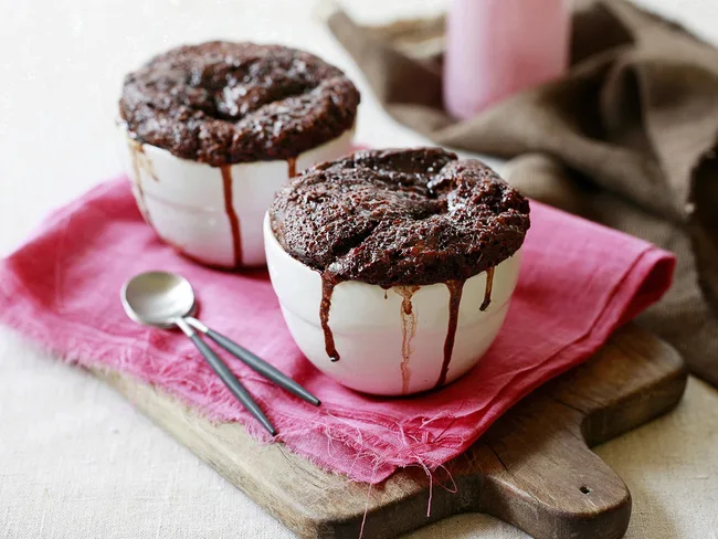 Two chocolate lava cakes in white bowls on pink cloth with spoons, perfect for Mother's Day treat.