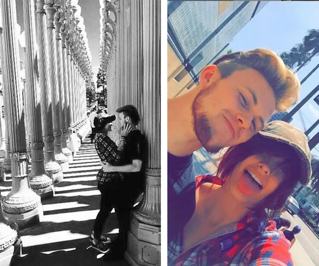 A couple poses affectionately between urban light poles and takes a playful selfie outside on a sunny day.