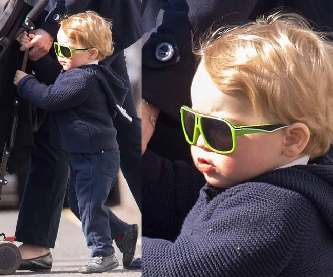 Young child in navy clothes and green sunglasses, standing beside an adult with a black stroller.