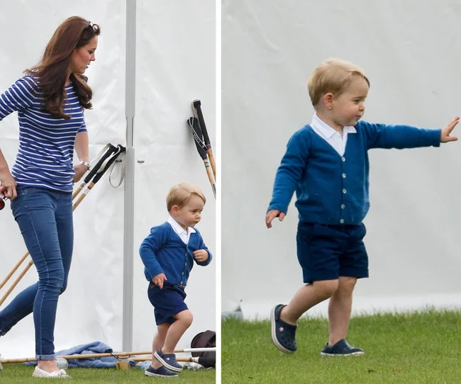 Toddler in blue cardigan playing on grass while a woman in stripes walks nearby.