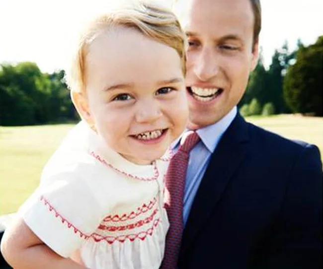 A young child smiling in front of an adult, both outdoors on a sunny day.