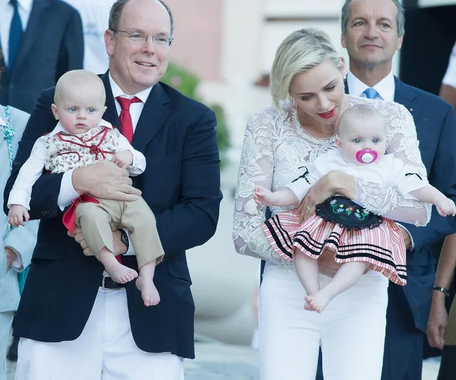 A man and woman holding two babies, one with a pacifier, in an outdoor setting.