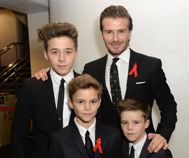 Father and three sons in suits with red ribbons, smiling at an event.