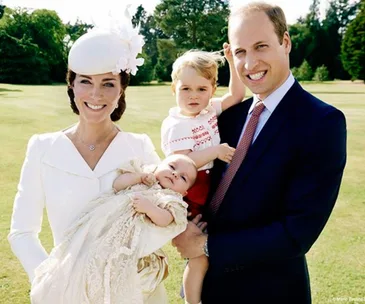 A family in formal attire poses outdoors in a sunny garden with two young children.