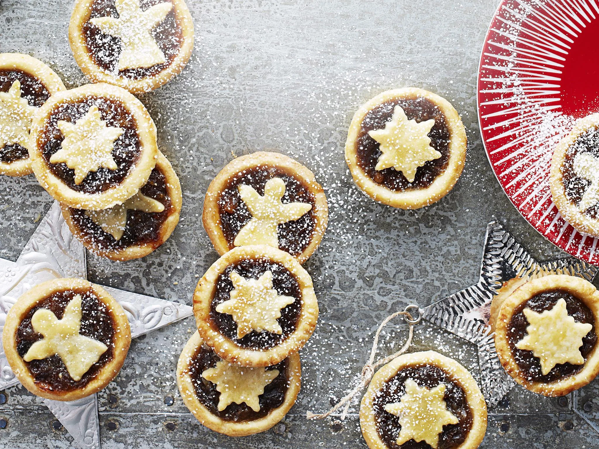 Assorted mince pies topped with star and angel pastry shapes, dusted with powdered sugar on a festive table setting.