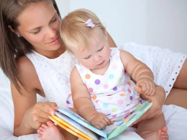 Mother and baby reading a colorful picture book on a bed.