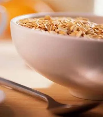 Bowl of cereal with milk and sprinkled oats, placed on a wooden table with a spoon beside it.