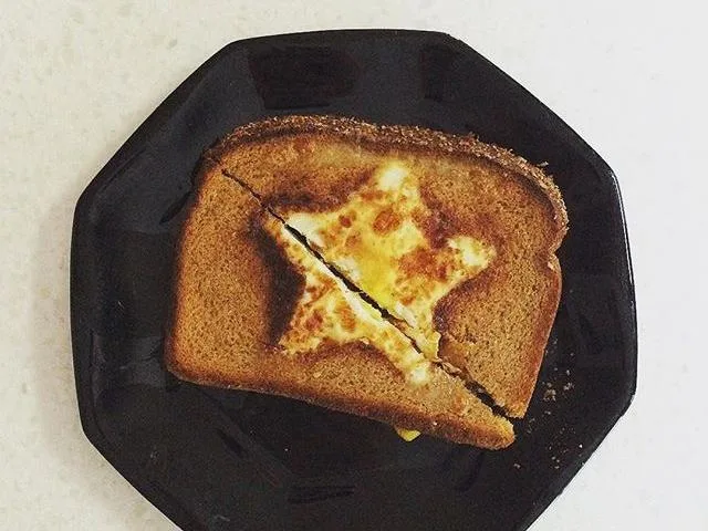 A piece of toast with a star-shaped egg in the center, slightly cracked, on a black plate.