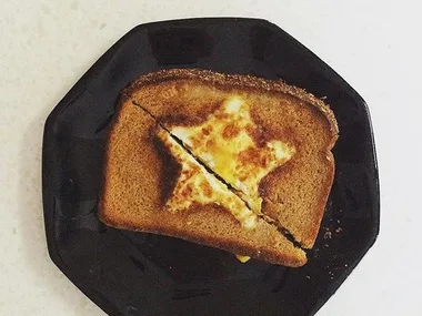 A piece of toast with a star-shaped egg in the center, slightly cracked, on a black plate.