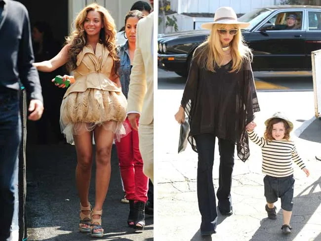Two women in stylish outfits; one with a beige dress, the other in a black poncho and hat, walking with a child.
