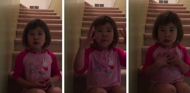 Young girl sits on stairs, speaking expressively, wearing pink pajamas with cartoon design.